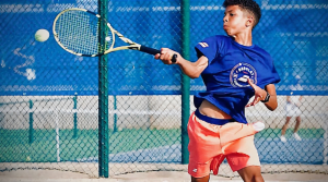 Action shot of student, Kyle Babbage, playing tennis outdoors.